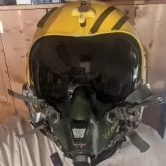 A person wearing a yellow and black pilot flight helmet with a tinted visor.