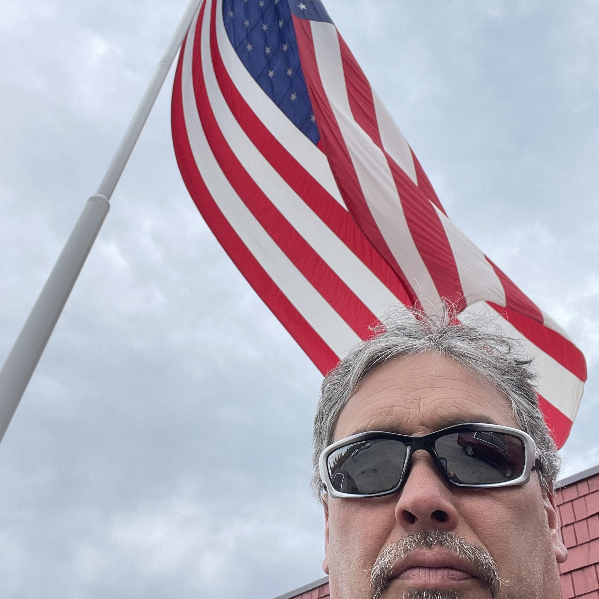A man standing proudly by an American flag who left a review for POH Group LLC, a trusted Loganville local home buyer and Gwinnett County home buyer. He shares his experience selling his inherited family property quickly as-is. Living in another state, he needed to sell fast and found the process smooth, efficient, and hassle-free